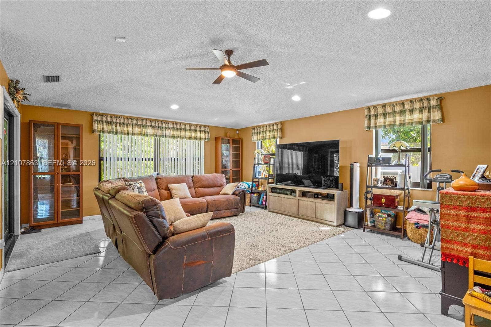 Living area featuring white ceramic tile flooring, a vaulted ceiling with a central fan, recessed lighting, and built-in wood cabinetry