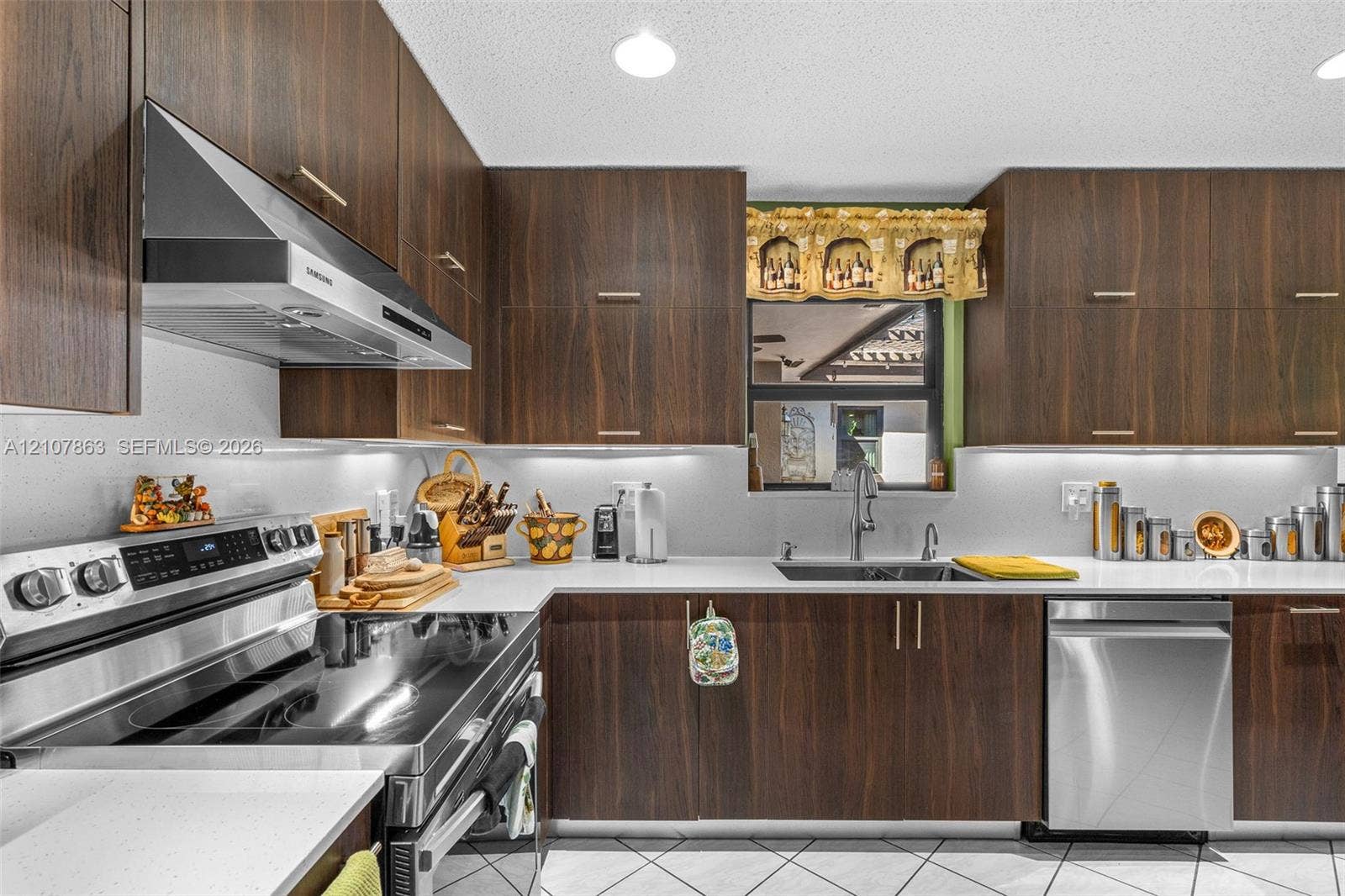 Kitchen featuring full-height dark wood-finish cabinetry, solid surface countertops, stainless steel appliances, a stainless steel undermount sink, and under-cabinet lighting