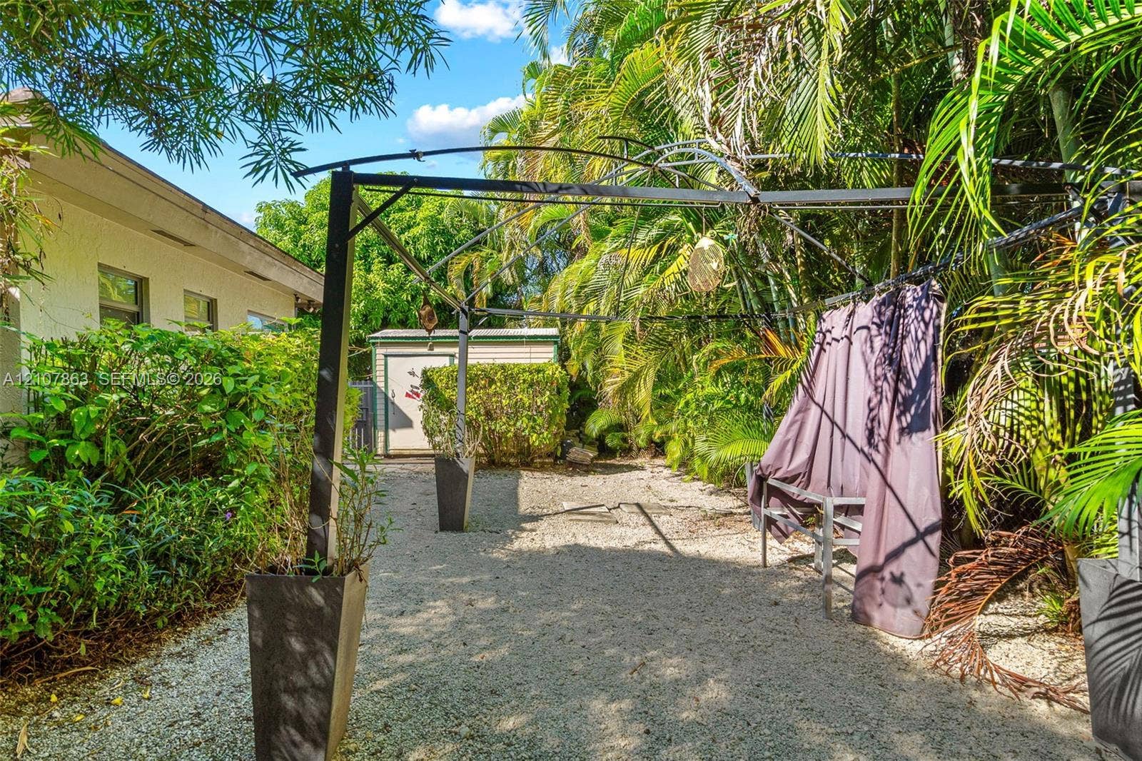 Exterior space featuring a gravel ground cover, a metal-framed pergola, a detached storage shed, and mature perimeter landscaping