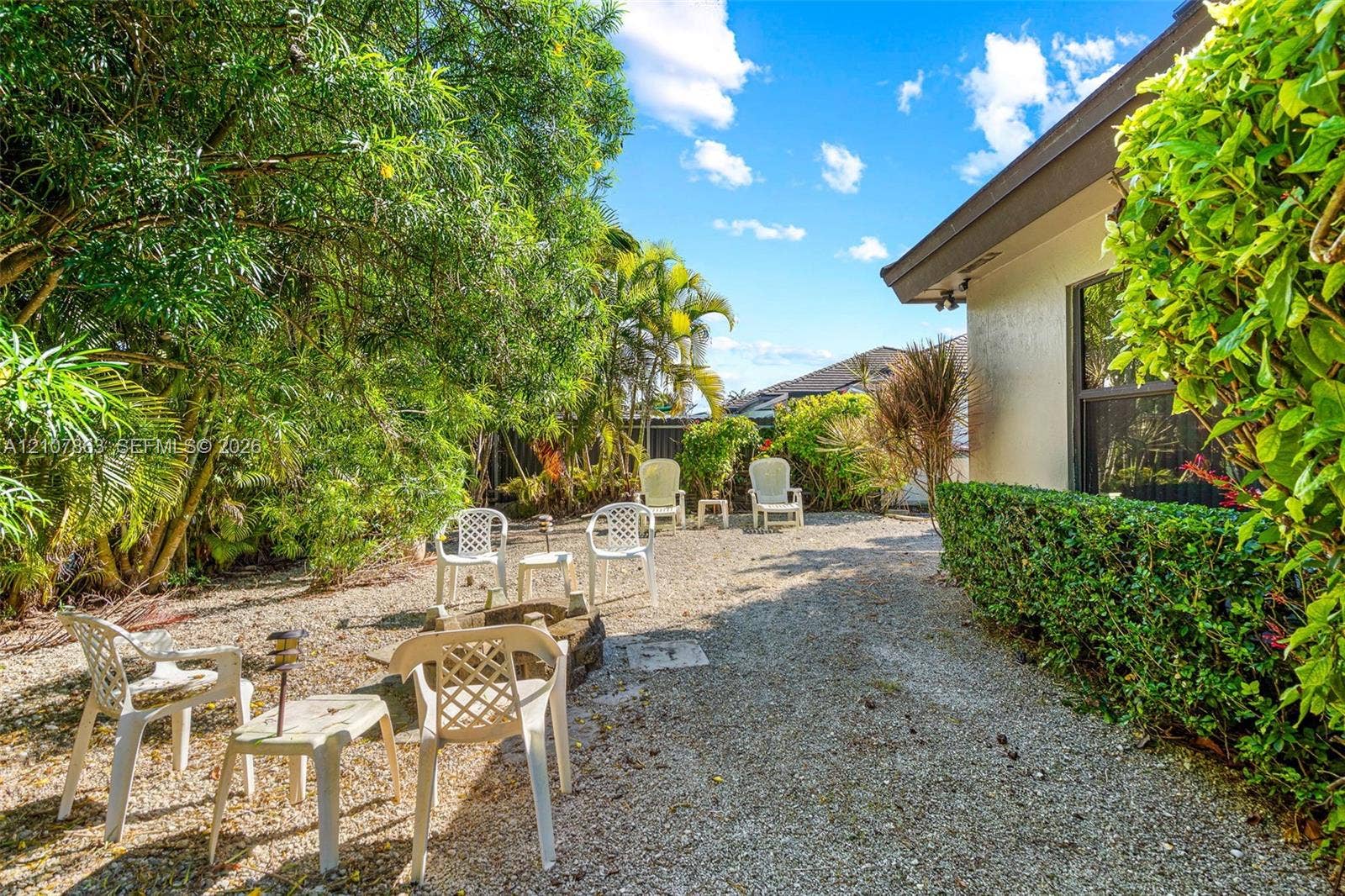 Backyard featuring a stone-aggregate ground cover, mature perimeter landscaping, palm trees, and structural stucco exterior wall