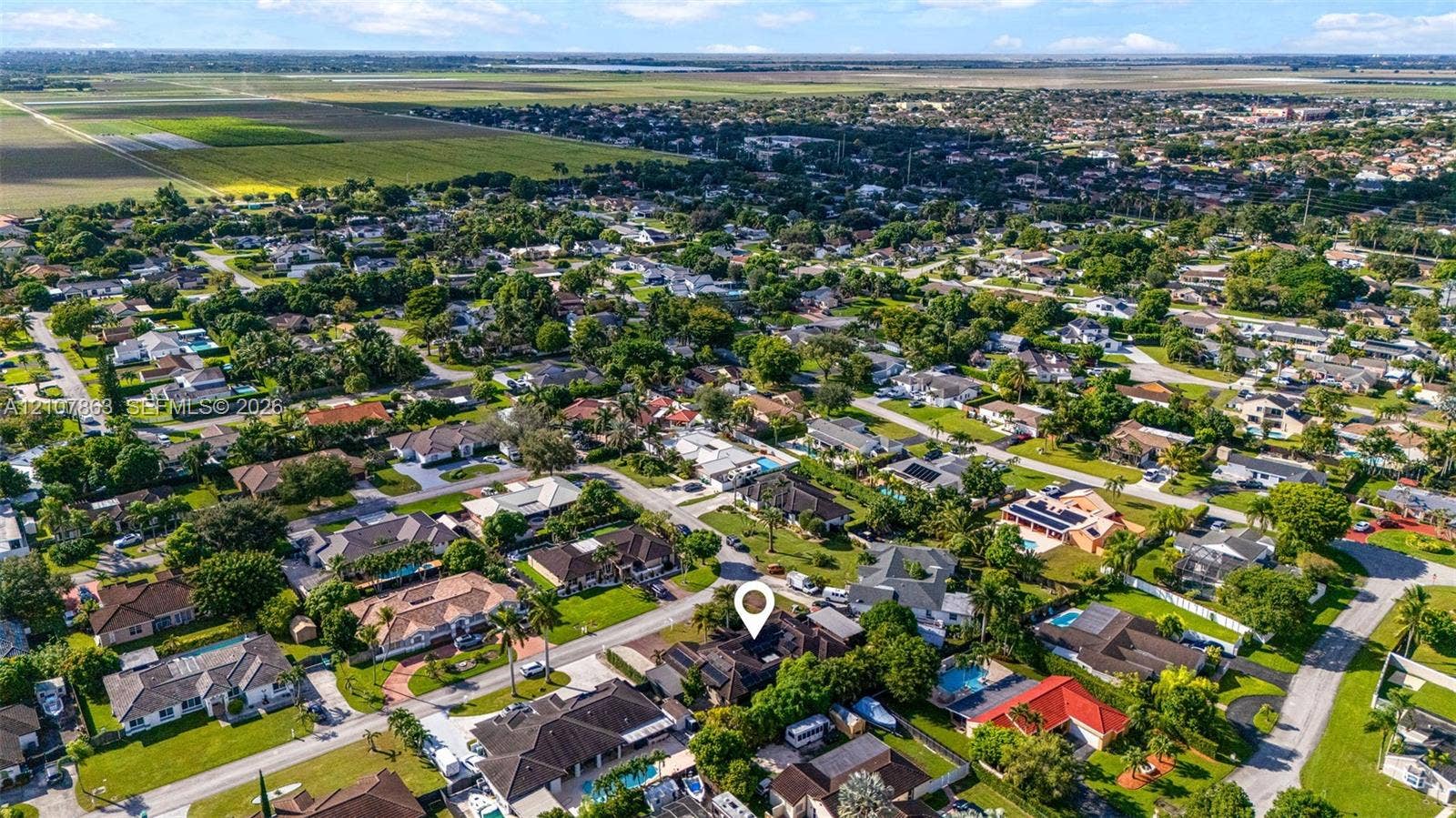 Aerial perspective of a residential property featuring a multi-pitched roof, paved driveway, mature perimeter landscaping, and established neighborhood infrastructure