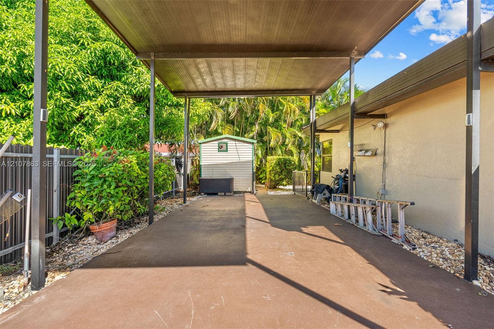 Covered carport featuring a concrete surface, metal framing, and a dedicated exterior storage structure