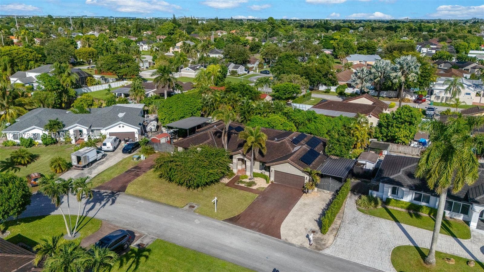 Aerial perspective of a single-story residence featuring a multi-pitched roof, roof-mounted solar panels, an integrated two-car garage, and a paved driveway