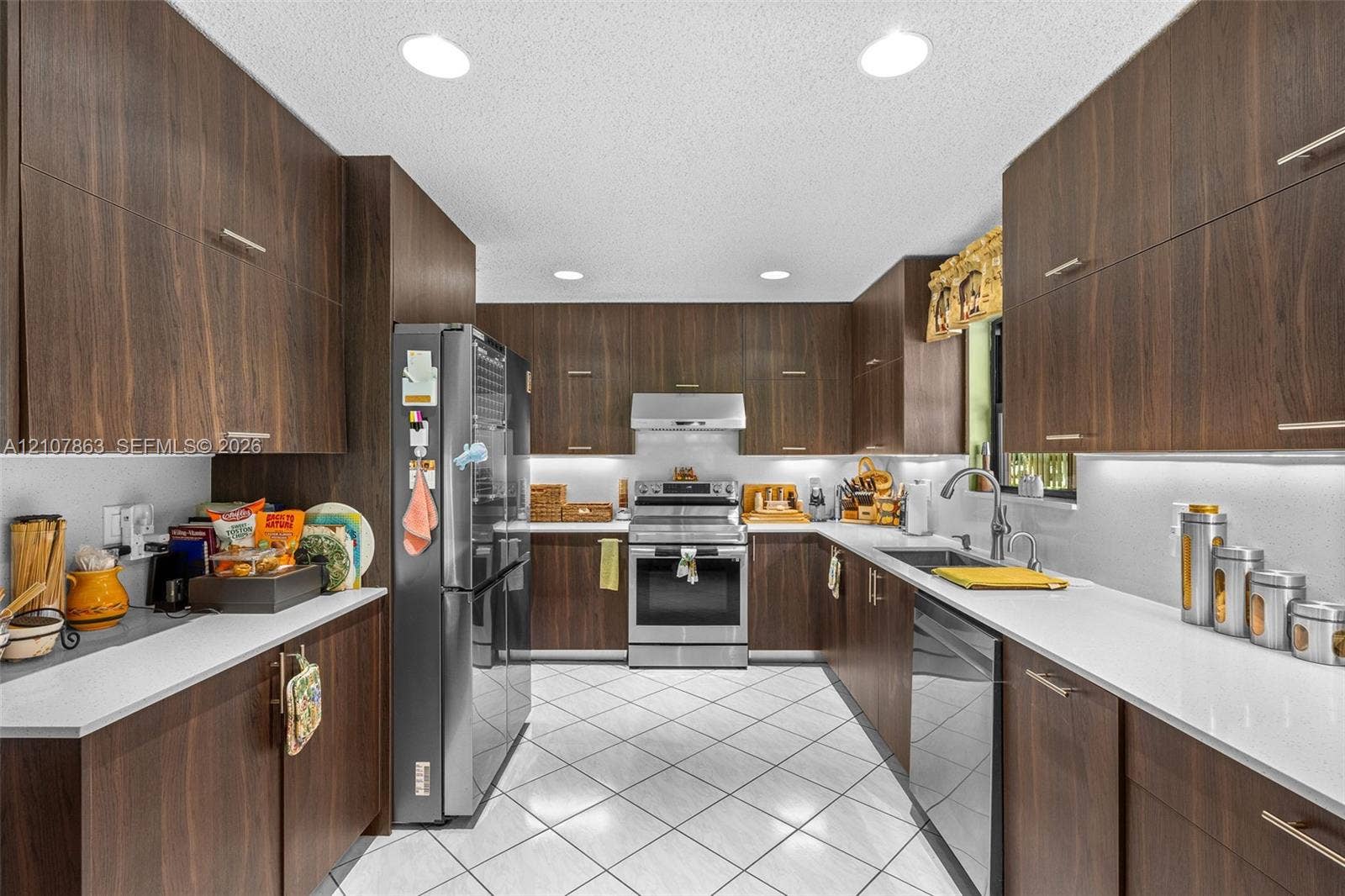 Kitchen featuring flat-panel wood-finish cabinetry, solid surface countertops, stainless steel appliances, tile flooring, and recessed lighting