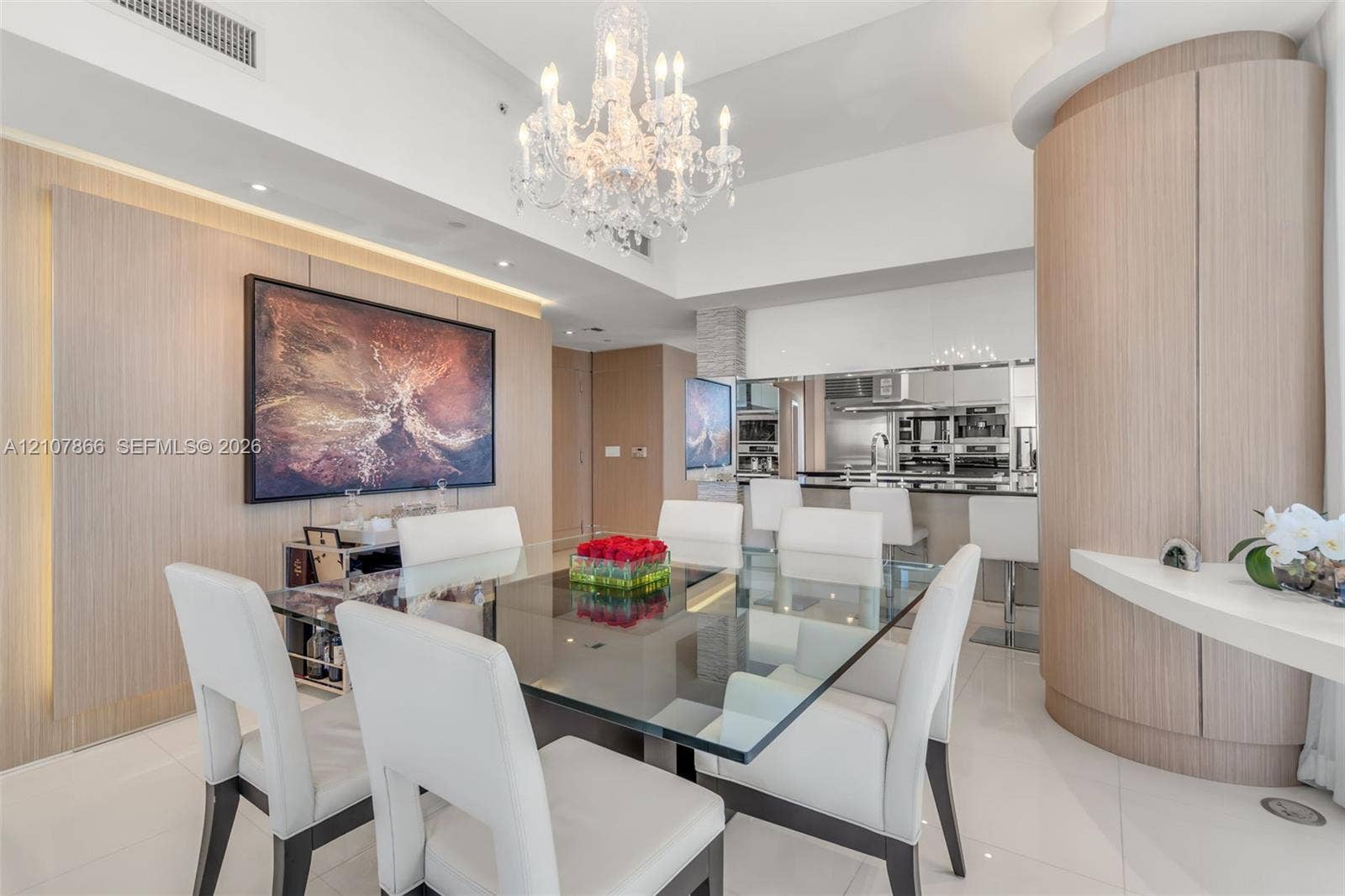 17121 Collins Avenue, #2608, Sunny Isles Beach, FL 33160 Formal dining area featuring a tiered crystal chandelier, wood-finish wall paneling, curved built-in cabinetry, and white polished flooring