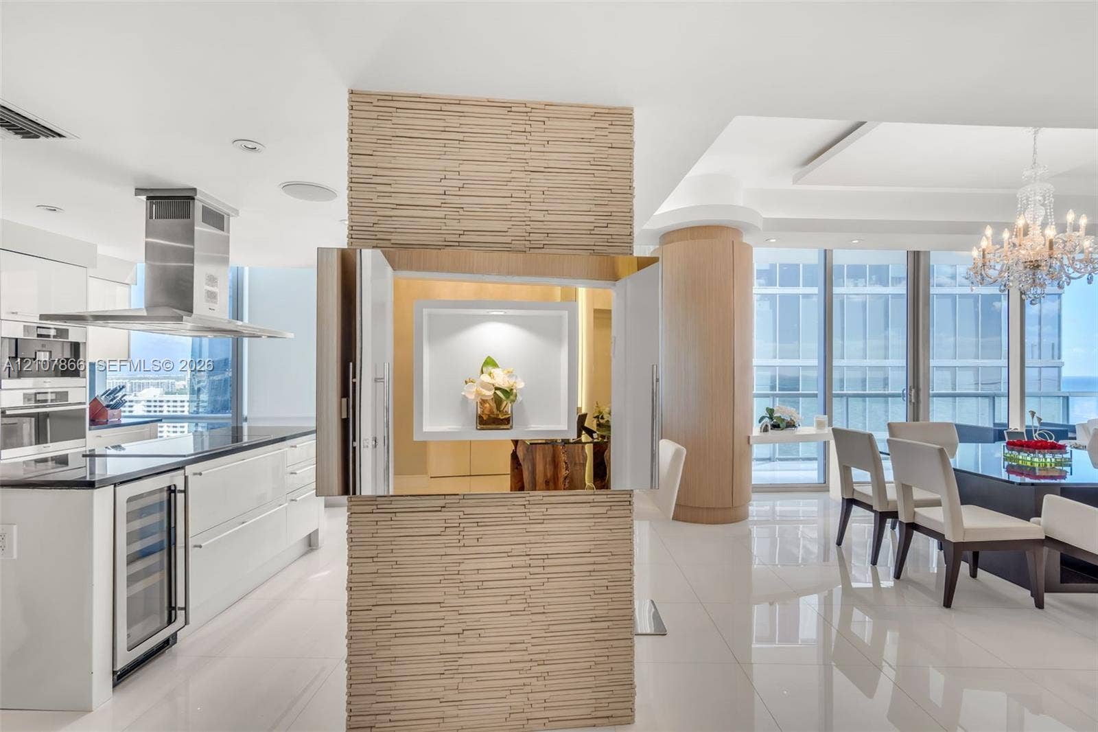 17121 Collins Avenue, #2608, Sunny Isles Beach, FL 33160 Stacked stone accent wall with a recessed display niche, white high-gloss cabinetry, stainless steel range hood, built-in wine refrigerator, and floor-to-ceiling windows