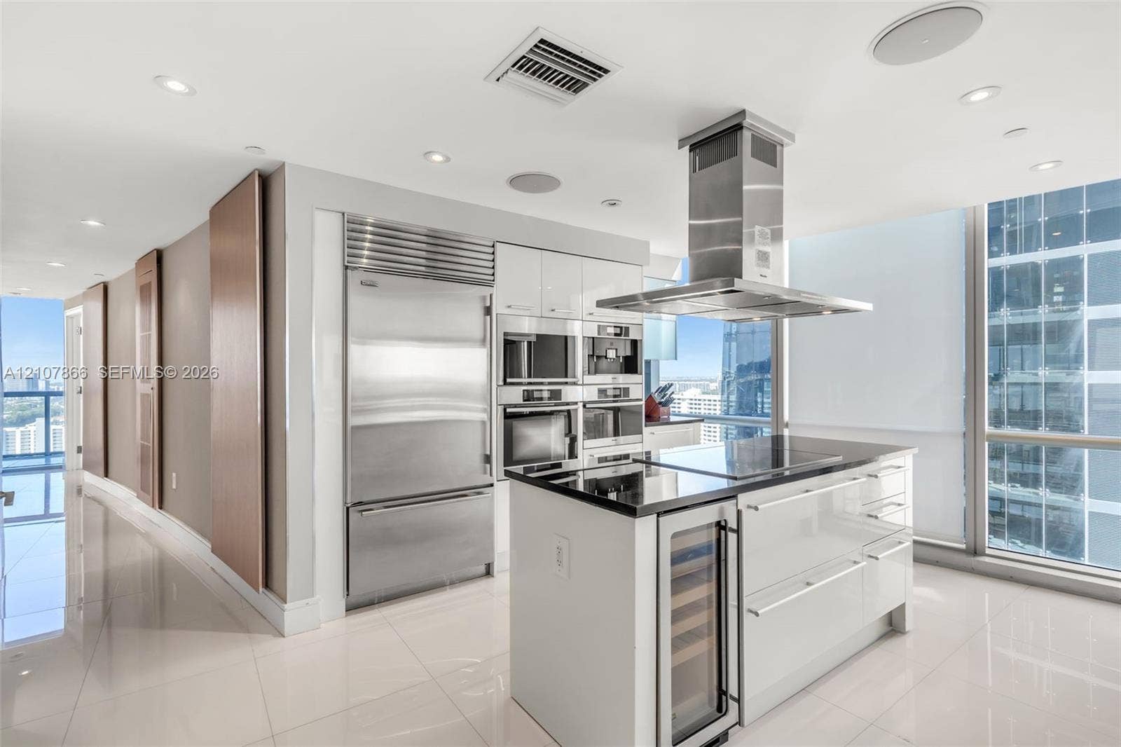 17121 Collins Avenue, #2608, Sunny Isles Beach, FL 33160 Modern kitchen featuring high-gloss cabinetry, stainless steel professional-grade appliances, a central island with a built-in wine refrigerator, a stone countertop, and floor-to-ceiling windows