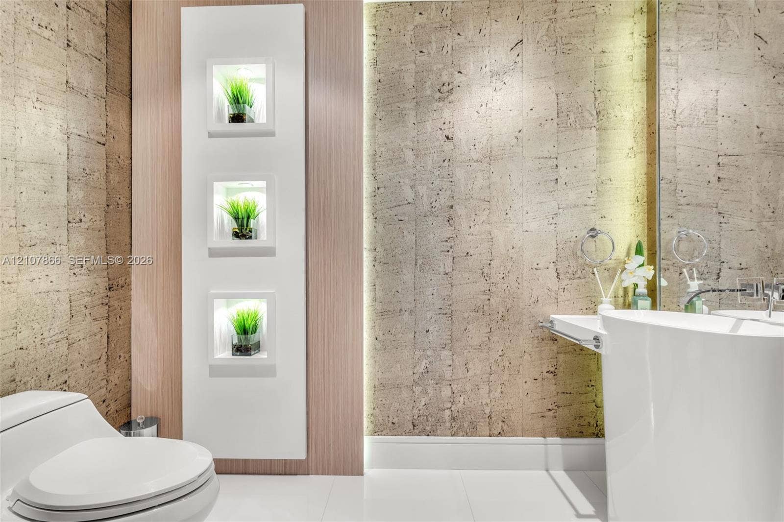 17121 Collins Avenue, #2608, Sunny Isles Beach, FL 33160 Textured stone-finish wall coverings, vertical built-in recessed shelving with integrated lighting, wood-finish paneling, white pedestal sink, and polished wall-mounted fixtures
