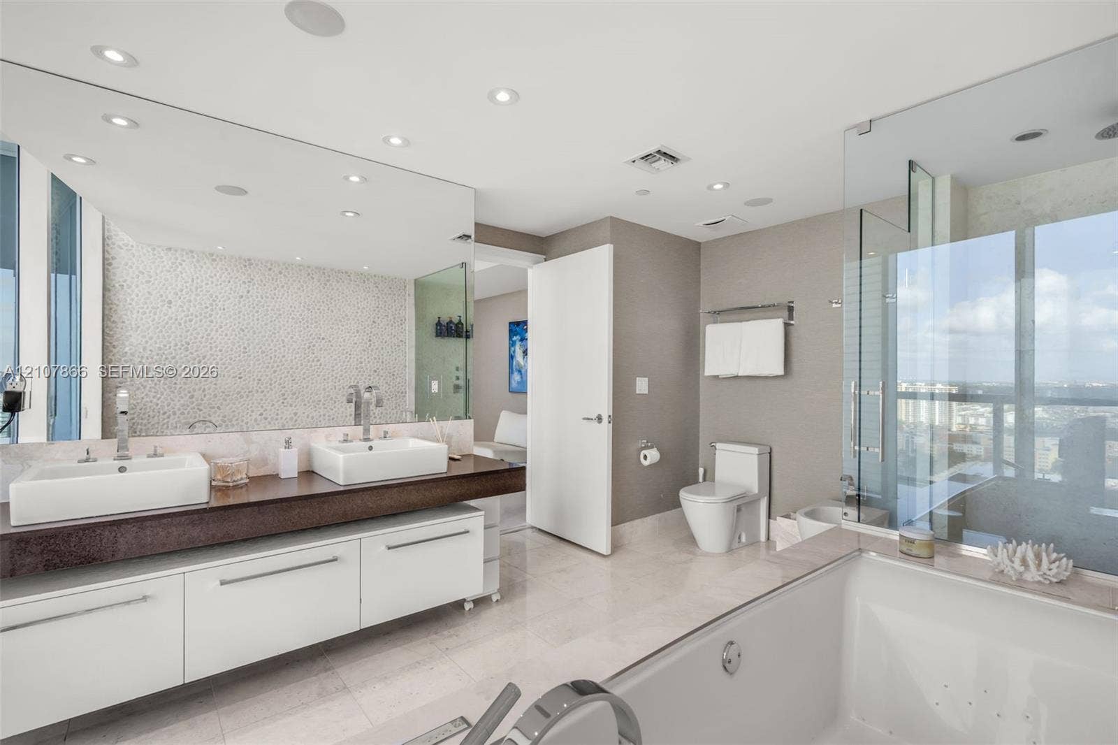 17121 Collins Avenue, #2608, Sunny Isles Beach, FL 33160 Floating double vanity with dual vessel sinks, full-width wall mirror, glass-enclosed shower, soaking tub, and stone tile flooring
