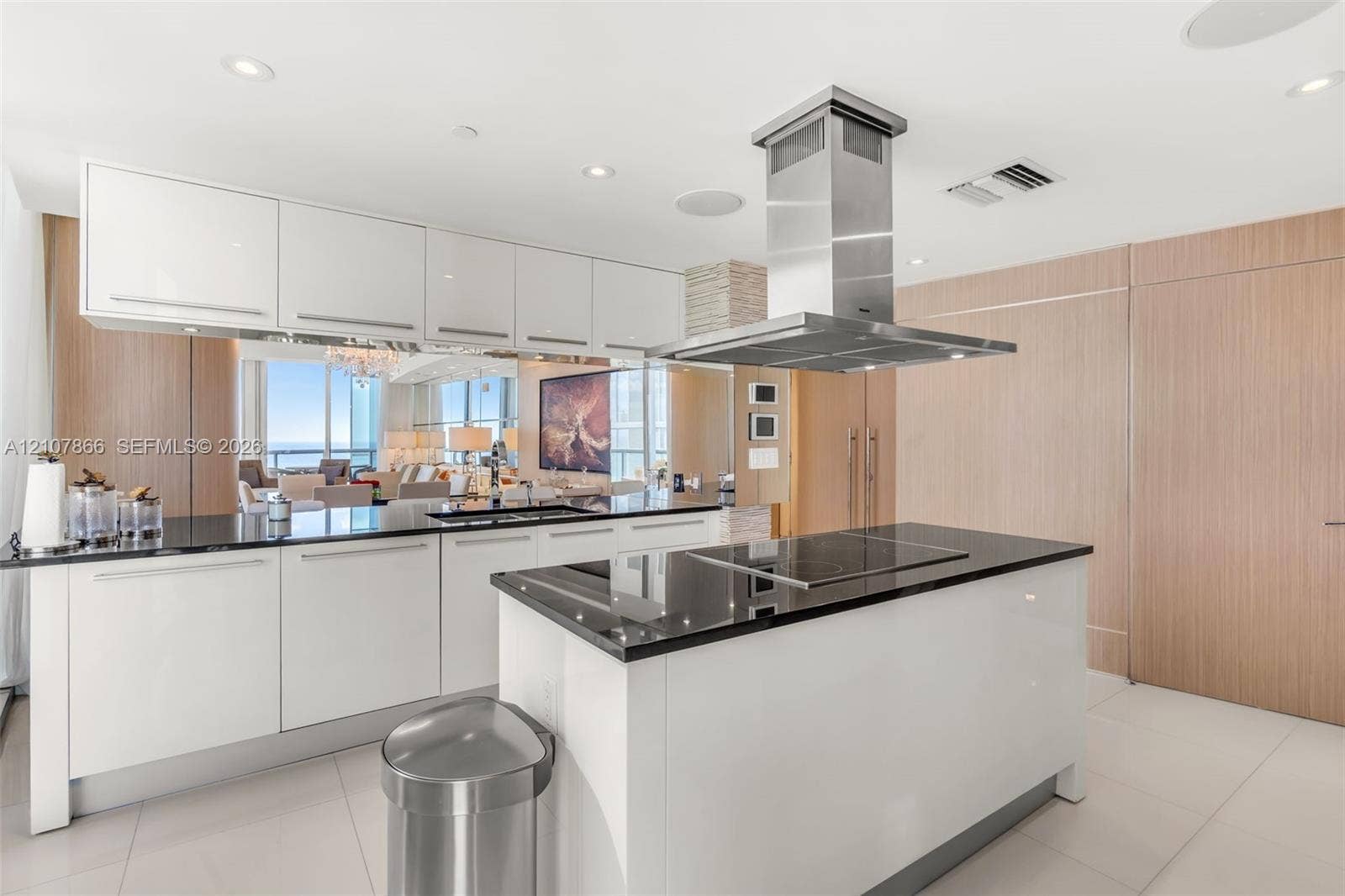 17121 Collins Avenue, #2608, Sunny Isles Beach, FL 33160 Modern kitchen featuring white flat-panel cabinetry, dark stone countertops, stainless steel island-mounted range hood, built-in cooktop, and wood-finish paneling