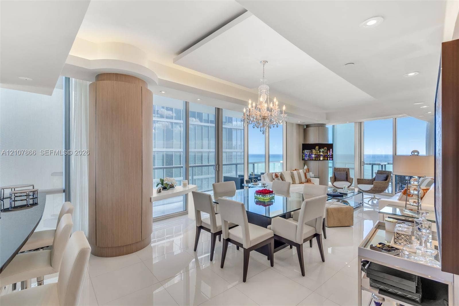 17121 Collins Avenue, #2608, Sunny Isles Beach, FL 33160 Open-concept interior featuring polished tile flooring, tray ceilings with recessed lighting, floor-to-ceiling glass windows, a circular wood-finish architectural column, and a crystal chandelier