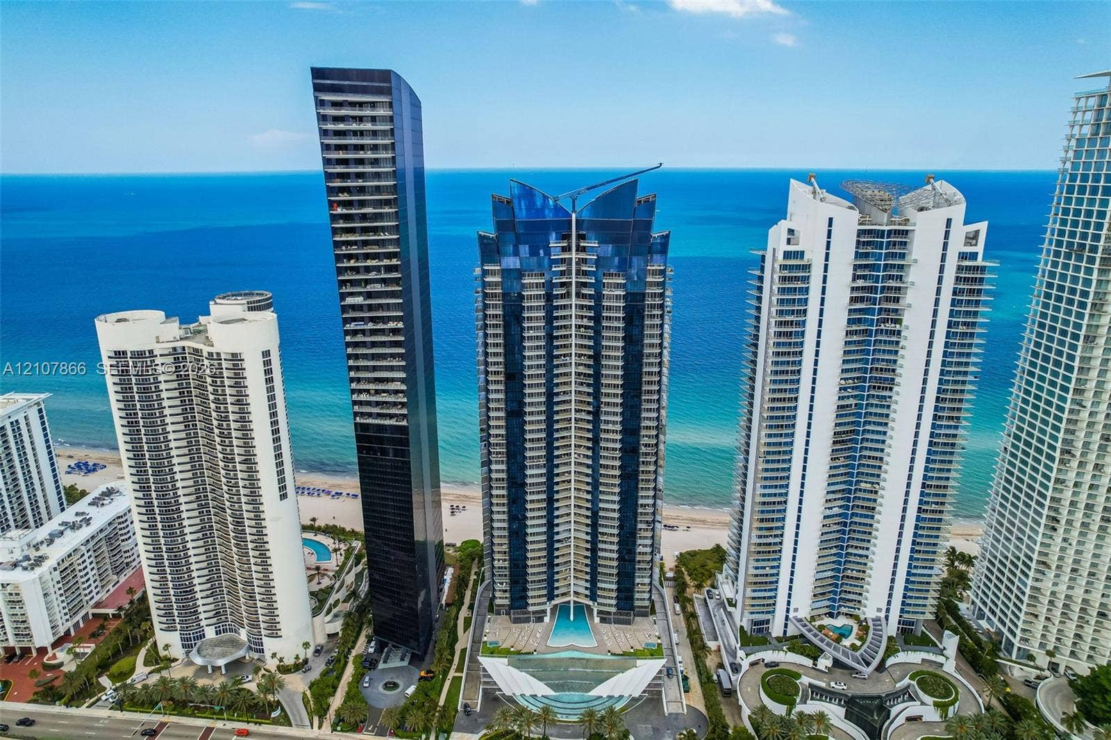 17121 Collins Avenue, #2608, Sunny Isles Beach, FL 33160 High-rise residential tower featuring a glass facade, private balconies, and an outdoor swimming pool situated along the beachfront