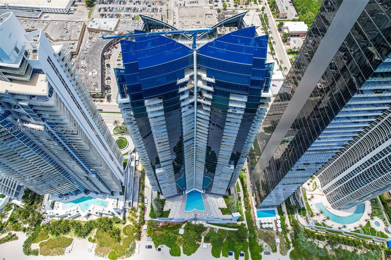 17121 Collins Avenue, #2608, Sunny Isles Beach, FL 33160 High-rise building featuring a glass facade, tiered balconies, and an outdoor swimming pool with surrounding landscaping