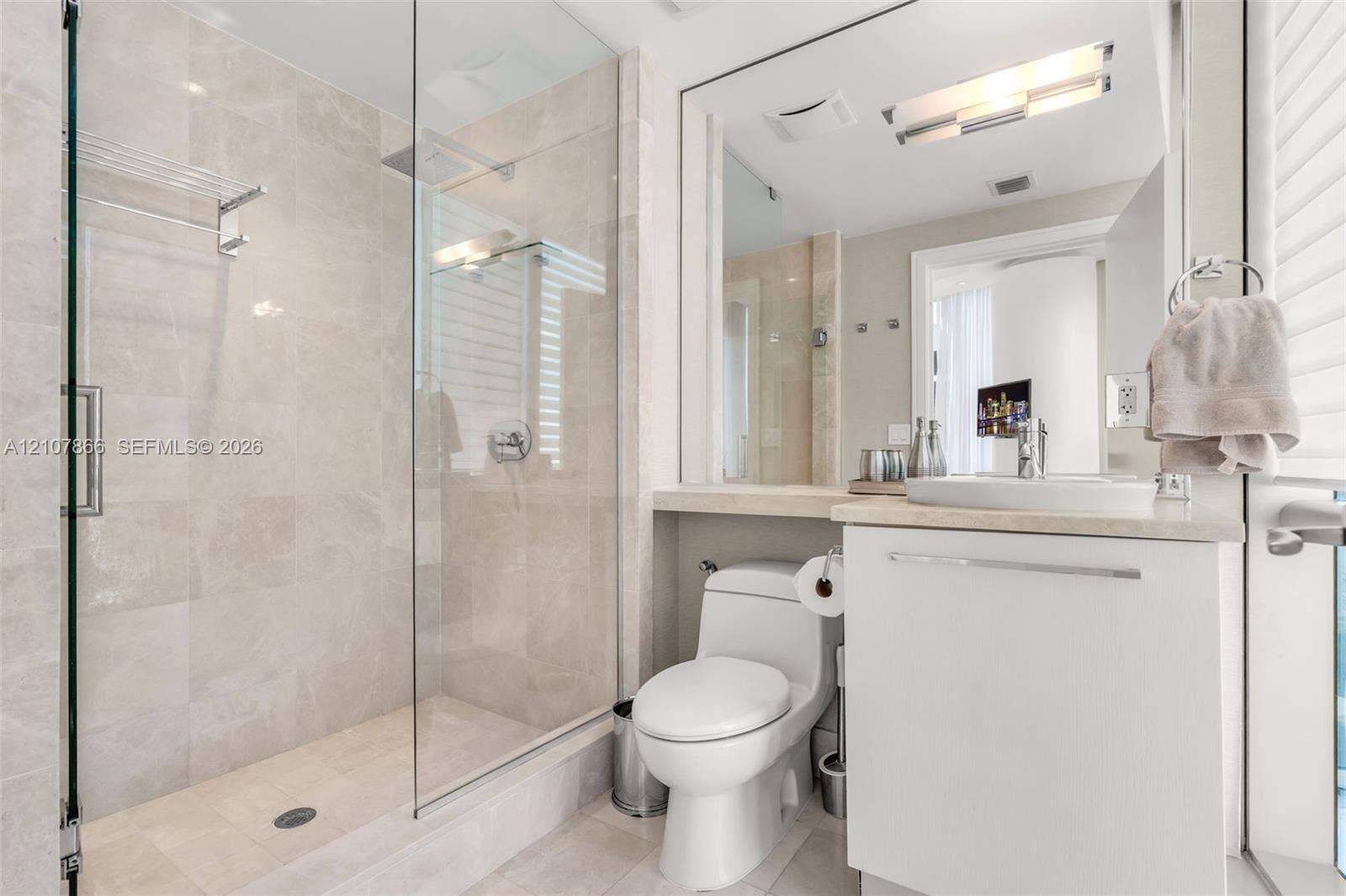 17121 Collins Avenue, #2608, Sunny Isles Beach, FL 33160 Glass-enclosed walk-in shower with tile surround, neutral-tone wall tile, white cabinetry, integrated sink, and large vanity mirror