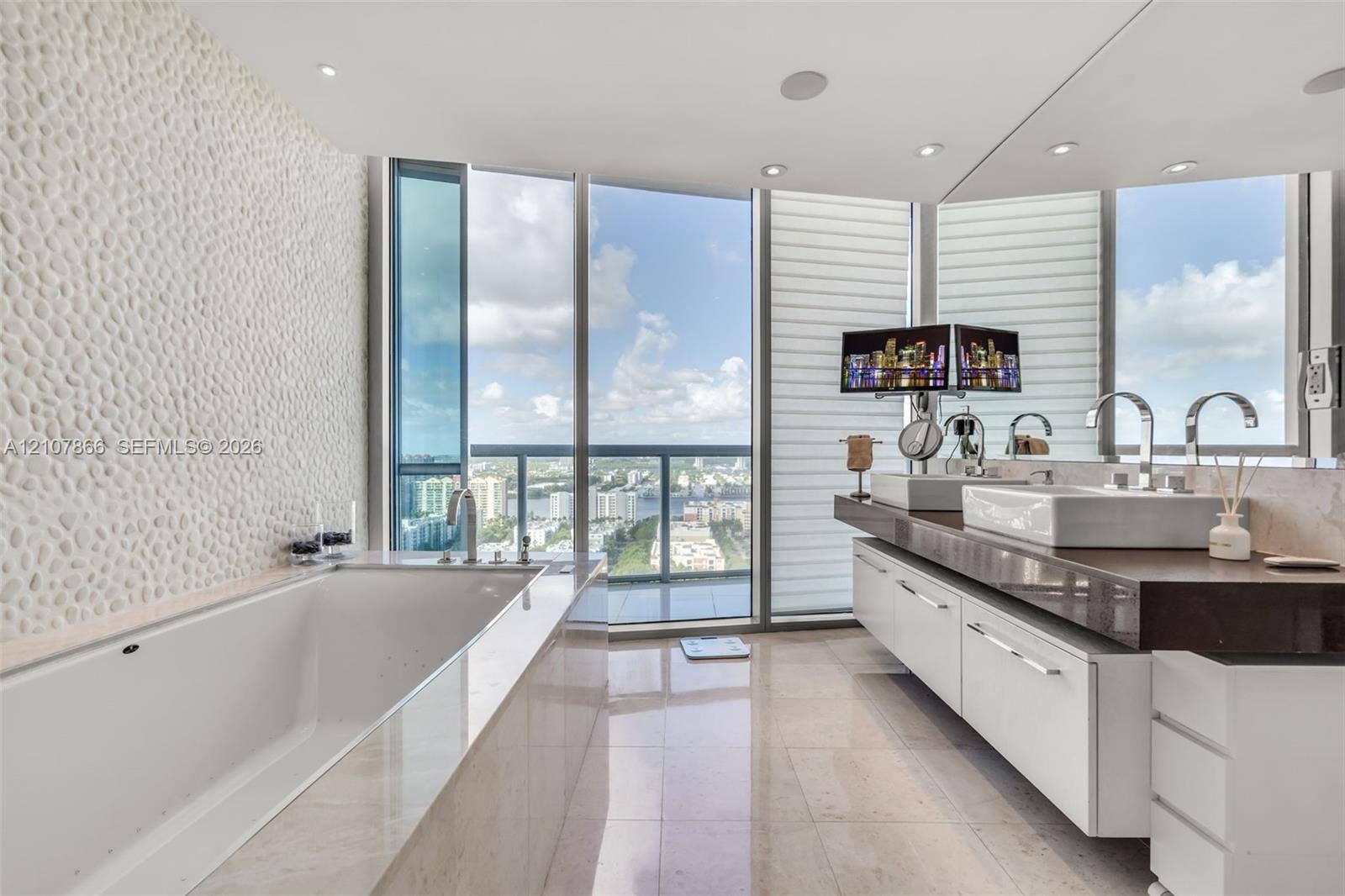 17121 Collins Avenue, #2608, Sunny Isles Beach, FL 33160 Bathroom featuring floor-to-ceiling windows, a deep soaking tub with a textured stone accent wall, a floating dual-sink vanity with a countertop, and recessed ceiling lighting