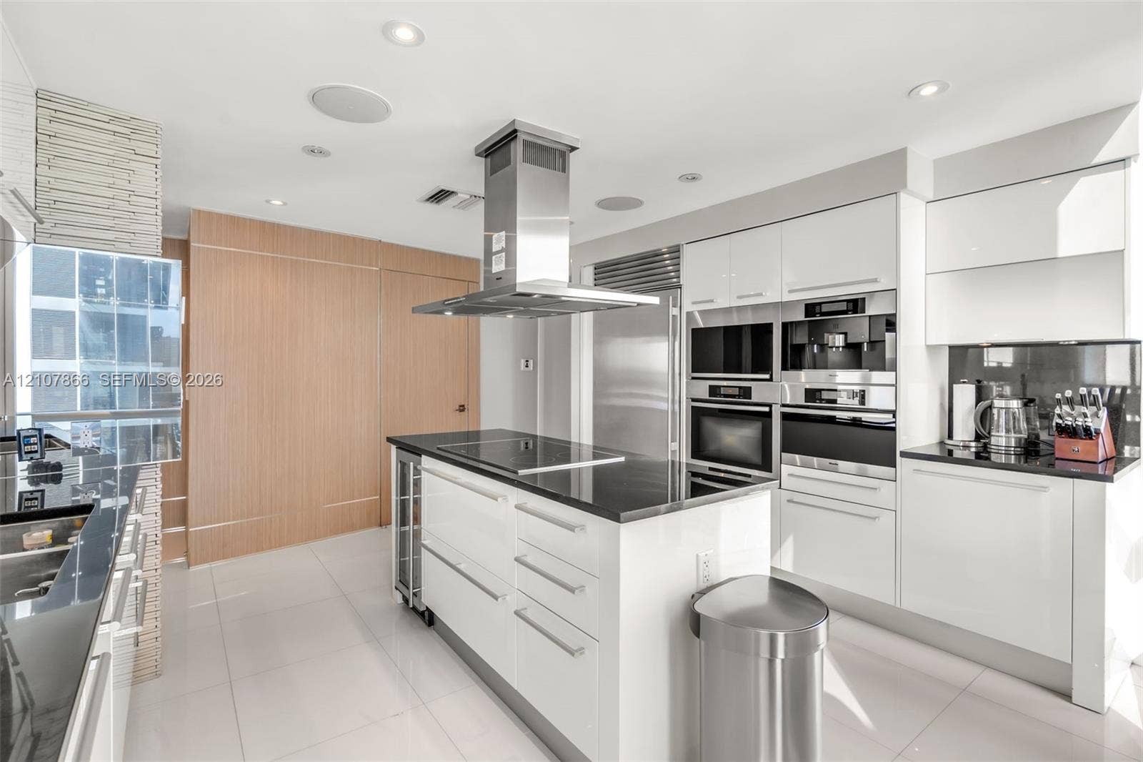 17121 Collins Avenue, #2608, Sunny Isles Beach, FL 33160 Contemporary kitchen featuring high-gloss white cabinetry, polished stone countertops, stainless steel professional-grade appliances, a central island with a glass-ceramic cooktop, and recessed ceiling lighting