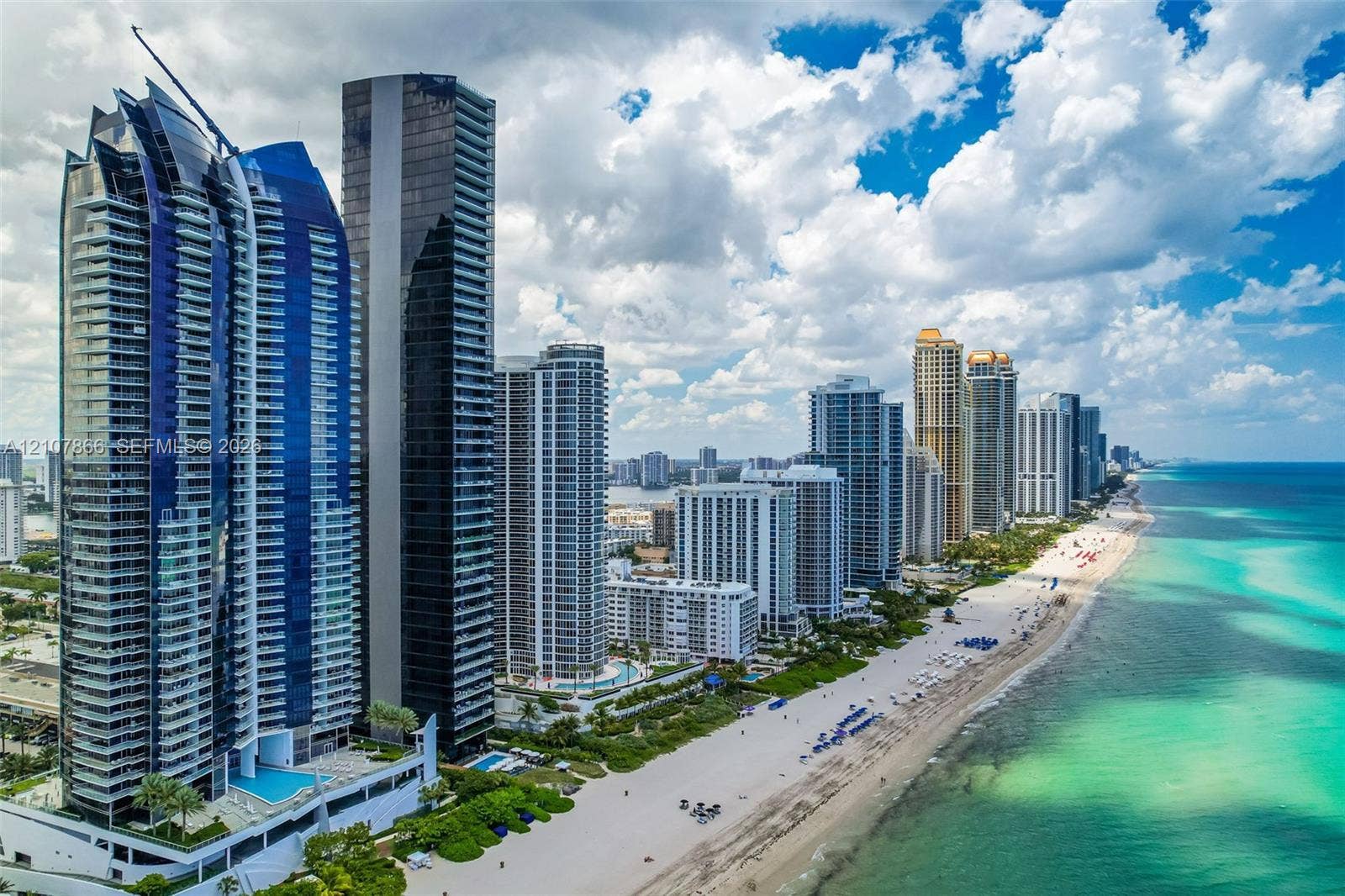 17121 Collins Avenue, #2608, Sunny Isles Beach, FL 33160 High-rise architecture featuring blue-tinted glass curtain walls and wrap-around balconies, situated directly on the Atlantic coastline with immediate beach access