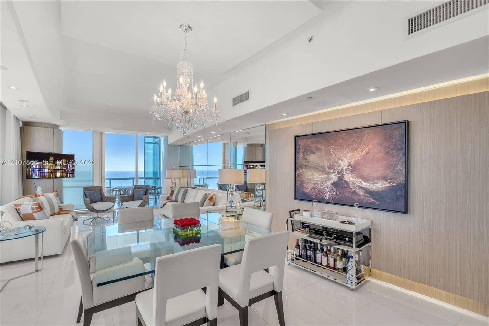 17121 Collins Avenue, #2608, Sunny Isles Beach, FL 33160 Expansive floor-to-ceiling glass windows, custom wood-paneled feature wall with integrated accent lighting, polished tile flooring, and decorative crystal chandelier