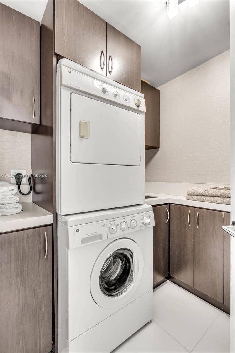 17121 Collins Avenue, #2608, Sunny Isles Beach, FL 33160 Laundry area featuring floor-to-ceiling dark-finish cabinetry, stacked washer and dryer unit, solid-surface countertops, and an integrated basin