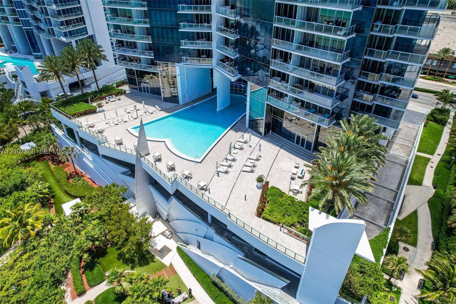 17121 Collins Avenue, #2608, Sunny Isles Beach, FL 33160 High-rise complex featuring an expansive elevated pool terrace, glass-railing balconies, stone-paver decking, and landscaped green spaces