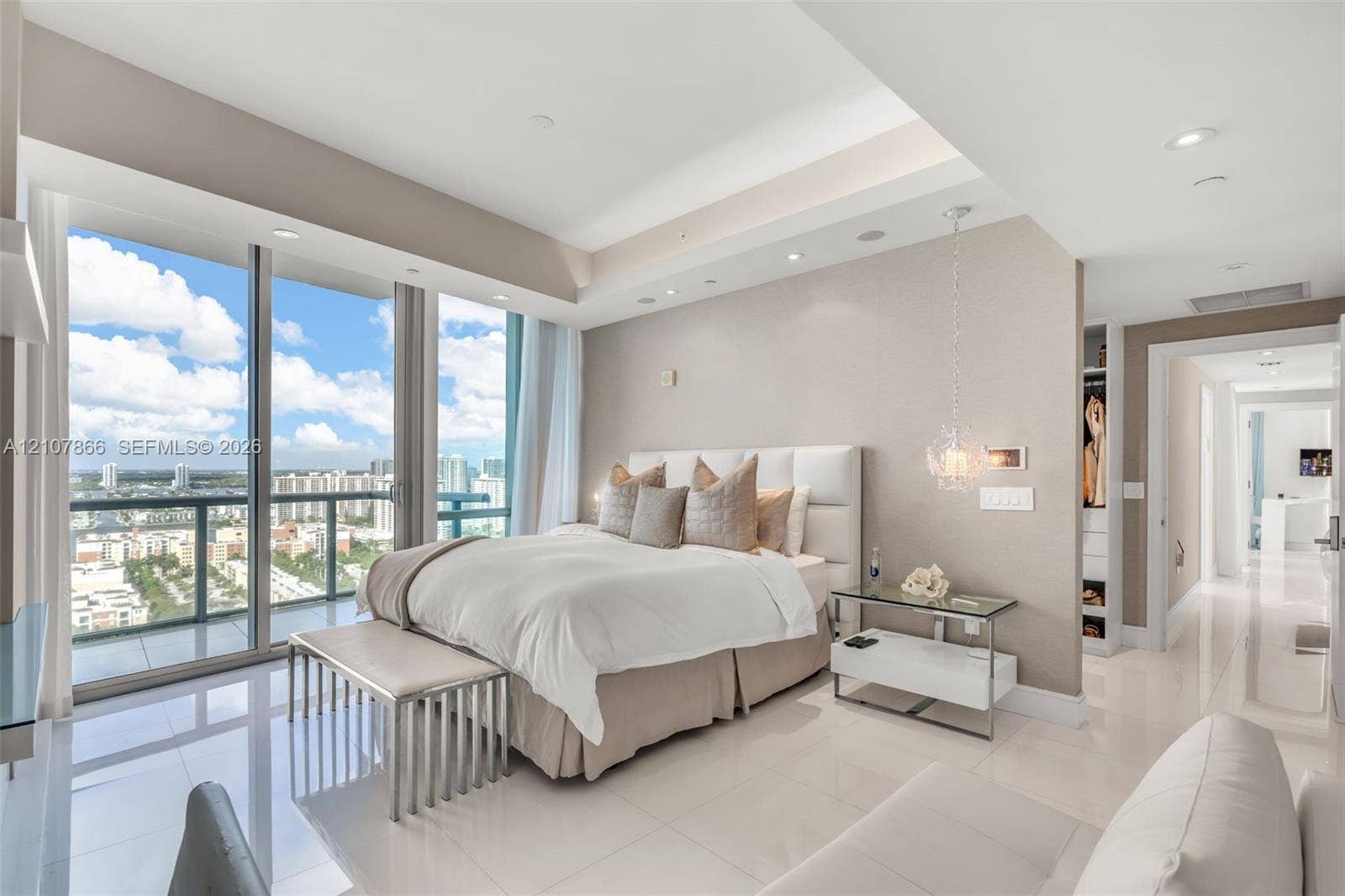 17121 Collins Avenue, #2608, Sunny Isles Beach, FL 33160 Floor-to-ceiling glass sliding doors, tray ceilings with recessed lighting, polished porcelain tile flooring, textured wall finishes, and a dedicated walk-in closet with custom built-in shelving