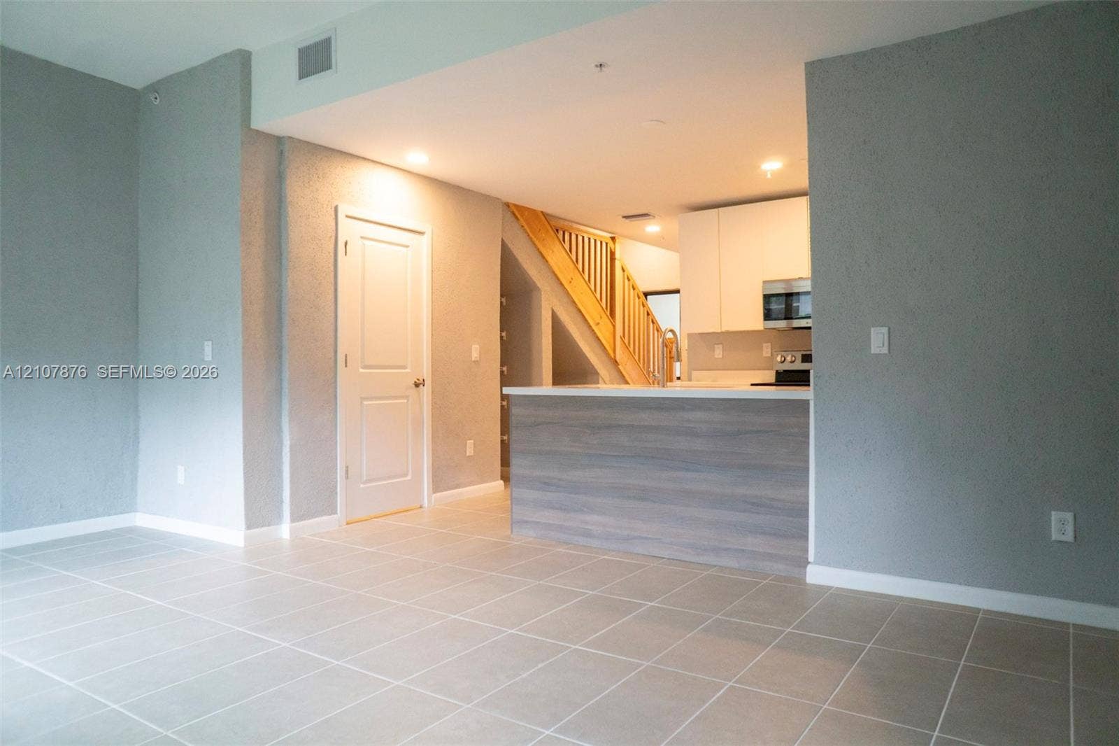 2526 Pierce Street, #8, Hollywood, Hollywood, FL 33020 Neutral tile flooring, kitchen island with wood-finish paneling, white flat-panel cabinetry, and staircase with wooden railings