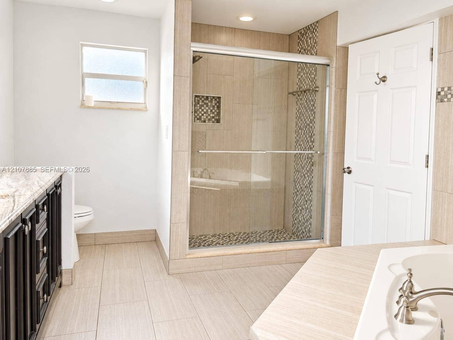 4840 NW 10th Terrace, Fort Lauderdale, Fort Lauderdale, FL 33309 Walk-in shower with sliding glass door, mosaic tile accent wall, built-in shower niche, light-toned floor tile, and dark wood-finish cabinetry with stone countertop