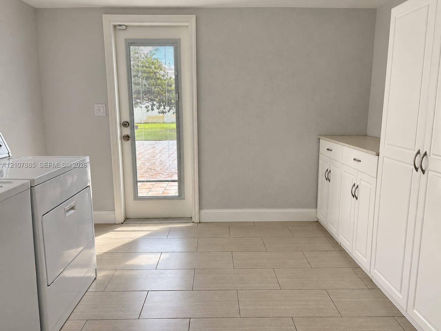 4840 NW 10th Terrace, Fort Lauderdale, Fort Lauderdale, FL 33309 Utility space featuring light-toned tile flooring, built-in white cabinetry with stone countertops, and a glass-paneled exterior door