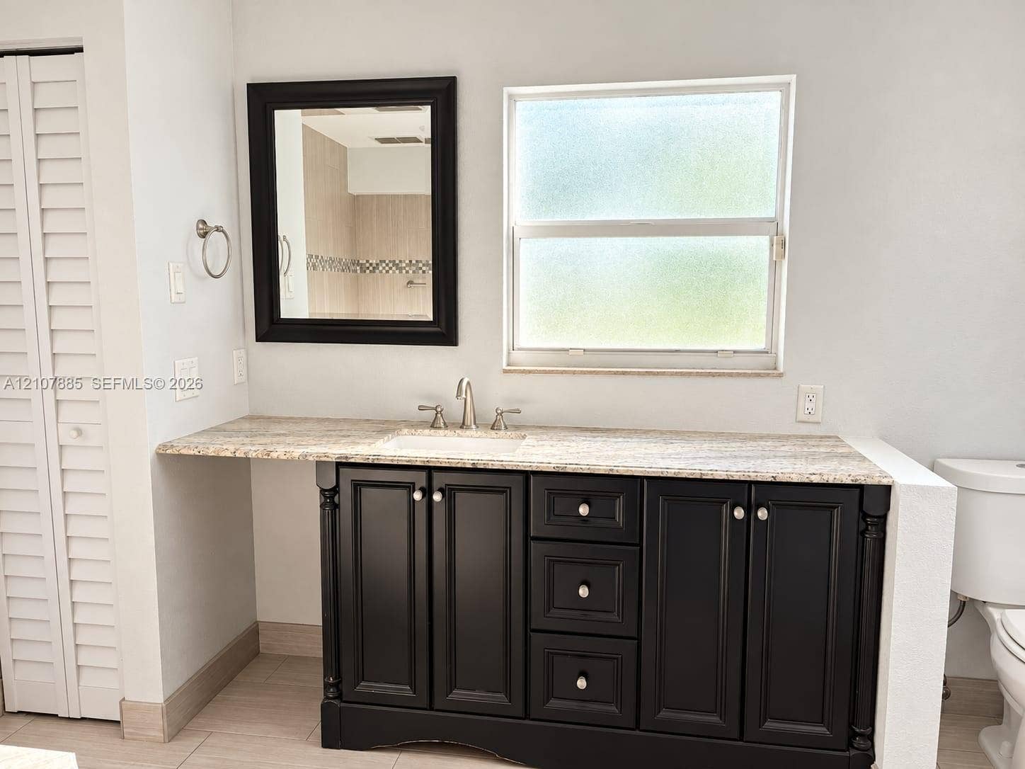 4840 NW 10th Terrace, Fort Lauderdale, Fort Lauderdale, FL 33309 Bathroom vanity featuring dark-finished cabinetry, a light-toned stone countertop, an integrated undermount sink, a framed wall mirror, and dual-handle metal faucet hardware