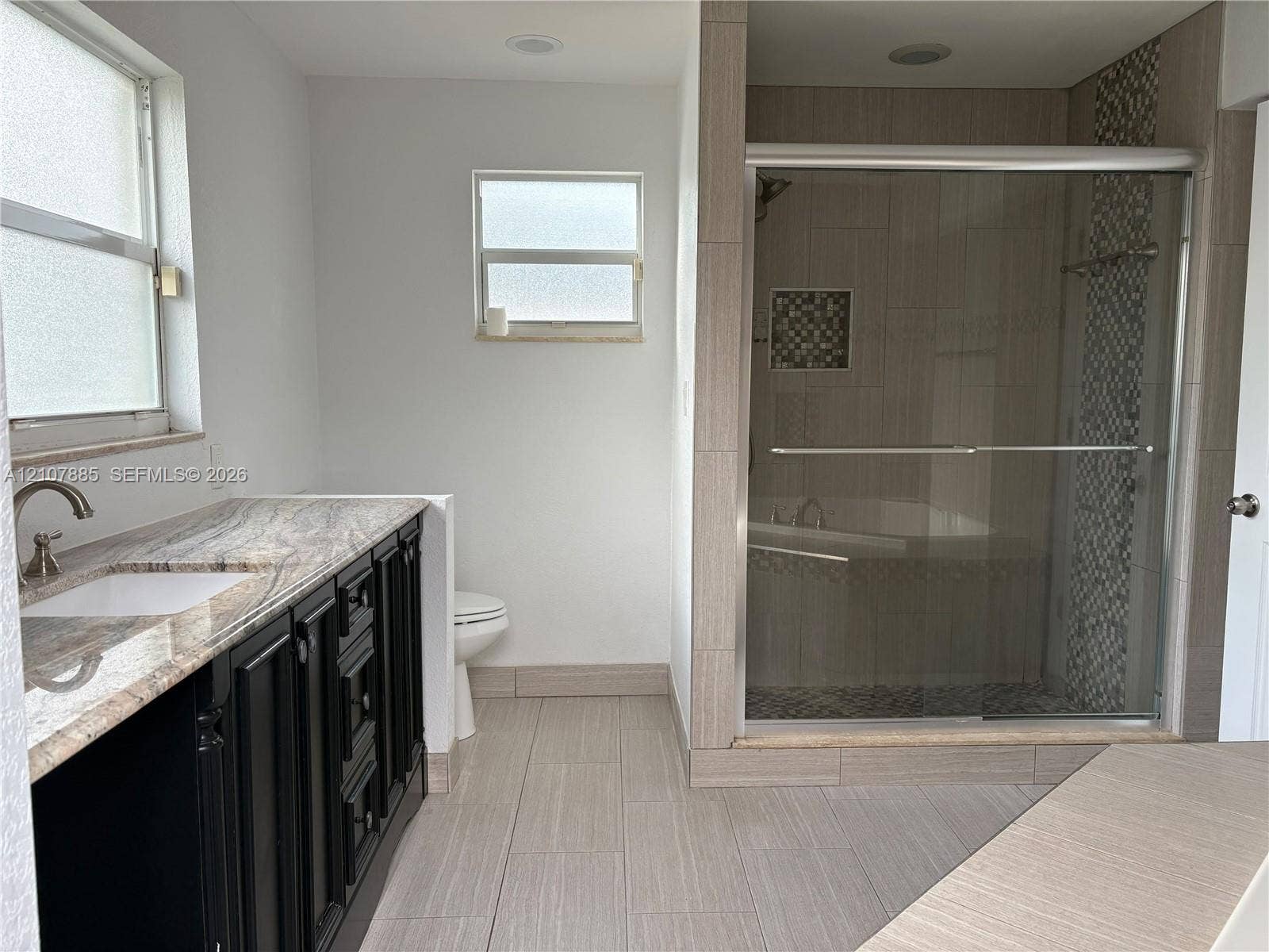 4840 NW 10th Terrace, Fort Lauderdale, Fort Lauderdale, FL 33309 Dark cabinetry vanity with stone-finish countertop, undermount sink, walk-in shower with sliding glass doors, mosaic tile accent, and light-tone floor tiling