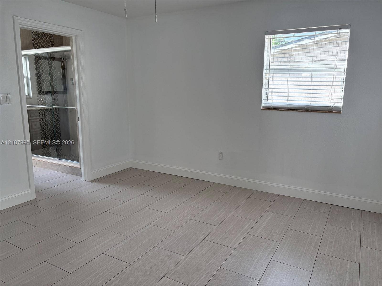 4840 NW 10th Terrace, Fort Lauderdale, Fort Lauderdale, FL 33309 Neutral-toned tile flooring, white wall finish, window with horizontal blinds, and doorway revealing a tiled shower enclosure with decorative mosaic accents