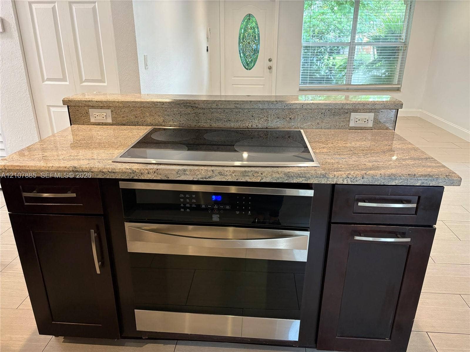 4840 NW 10th Terrace, Fort Lauderdale, Fort Lauderdale, FL 33309 Kitchen island featuring a stone countertop, integrated electric cooktop, stainless steel oven, and dark-toned cabinetry with metal hardware