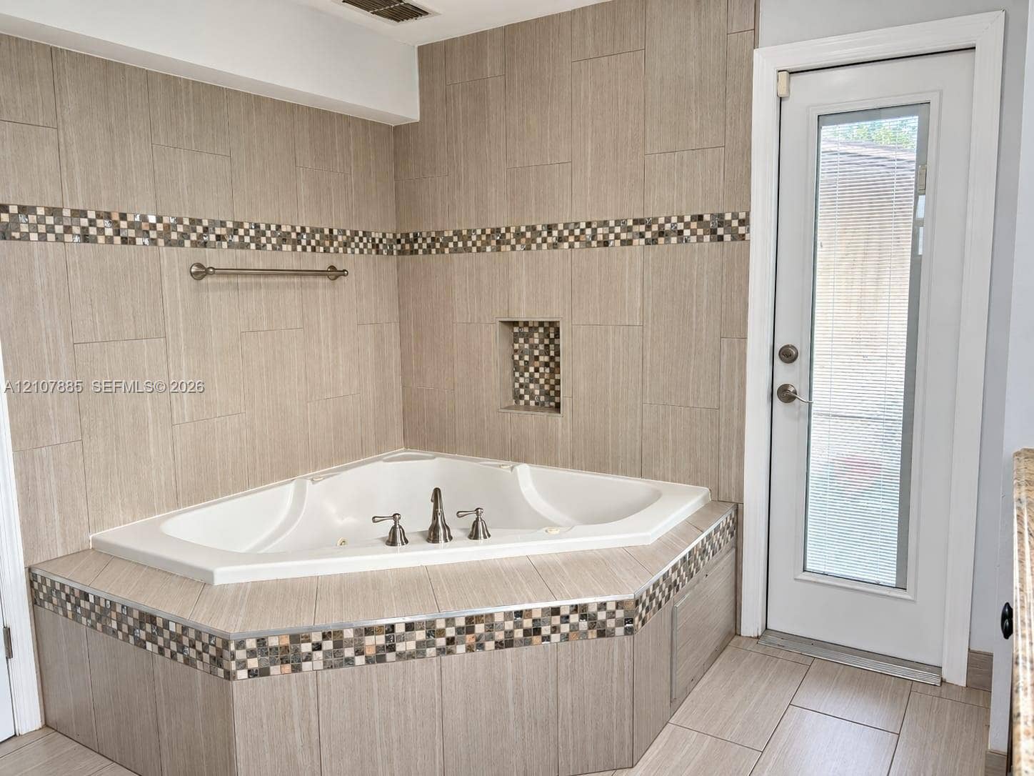 4840 NW 10th Terrace, Fort Lauderdale, Fort Lauderdale, FL 33309 Corner soaking tub featuring a tiled surround, recessed wall niche, multi-colored accent tile detailing, and a glass-paneled exterior door