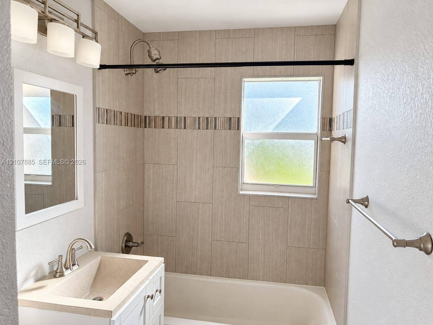 4840 NW 10th Terrace, Fort Lauderdale, Fort Lauderdale, FL 33309 Bathroom featuring a white vanity with an integrated countertop, wall-mounted light fixture, tiled shower surround with decorative accent inlay, and obscured glass window