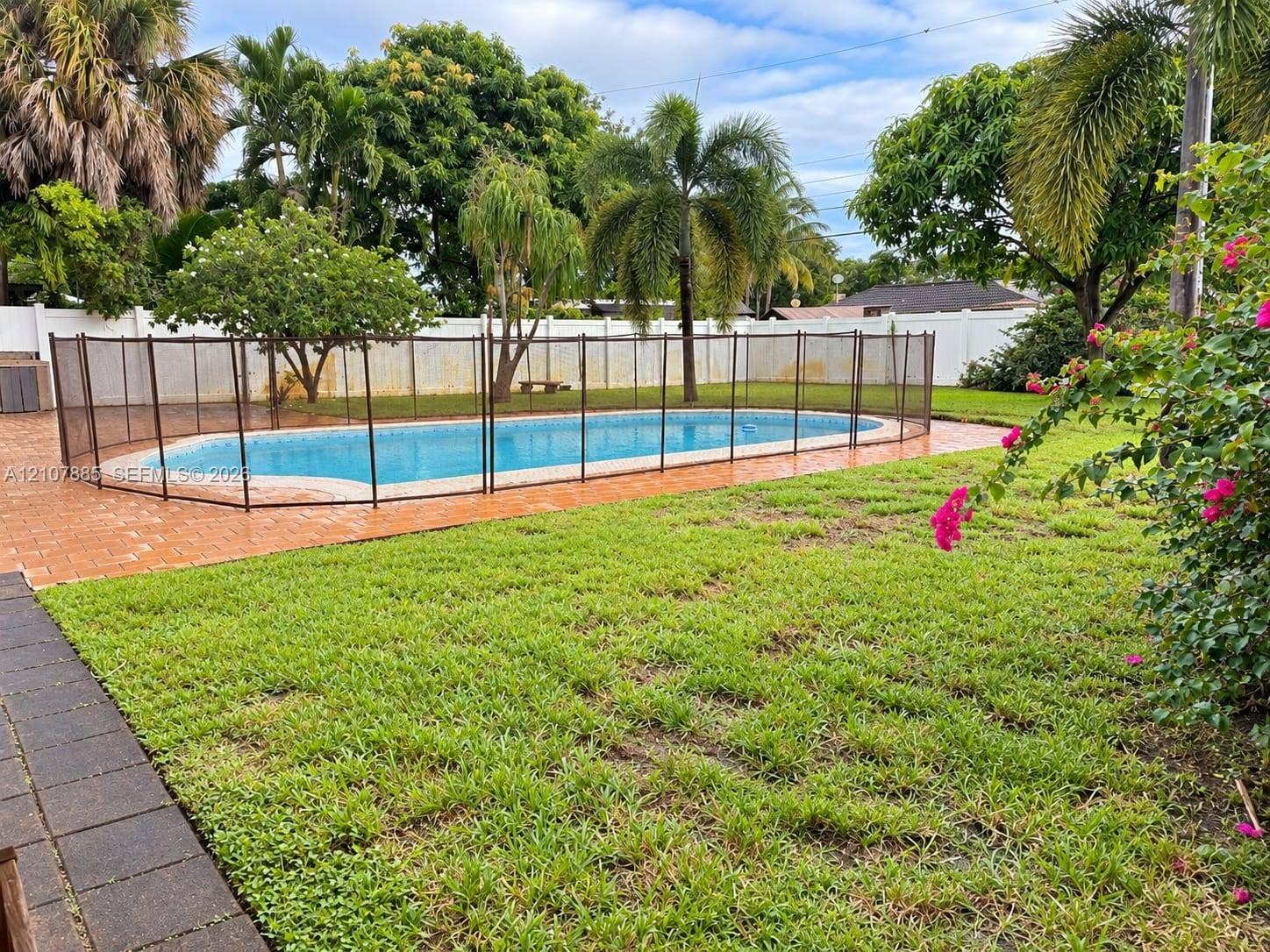 4840 NW 10th Terrace, Fort Lauderdale, Fort Lauderdale, FL 33309 Backyard featuring an in-ground swimming pool, mesh safety fencing, paved patio, expansive lawn, and white perimeter privacy fencing