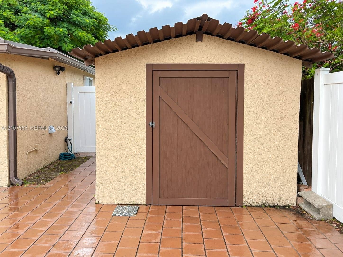4840 NW 10th Terrace, Fort Lauderdale, Fort Lauderdale, FL 33309 Stucco exterior storage structure featuring a single-panel door with wood-finish trim, a corrugated roof, and matching tiled patio flooring