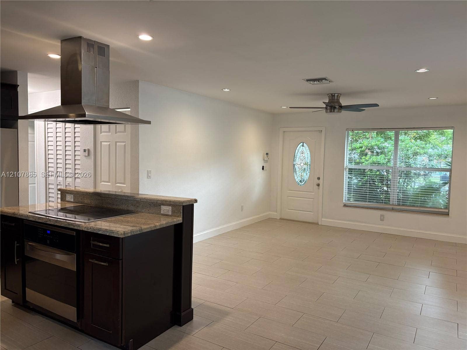 4840 NW 10th Terrace, Fort Lauderdale, Fort Lauderdale, FL 33309 Kitchen peninsula featuring stone-finish countertops, stainless steel chimney-style range hood, dark-toned cabinetry, ceramic tile flooring, and recessed lighting