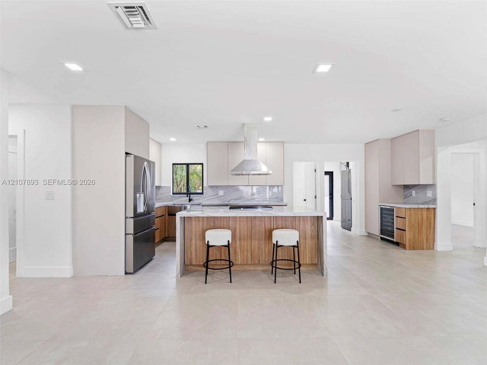 610 NE 164th Terrace, Miami, FL 33162 Kitchen featuring a central island with wood-finish cabinetry, stone countertops, stainless steel appliances, a range hood, and large-format tile flooring