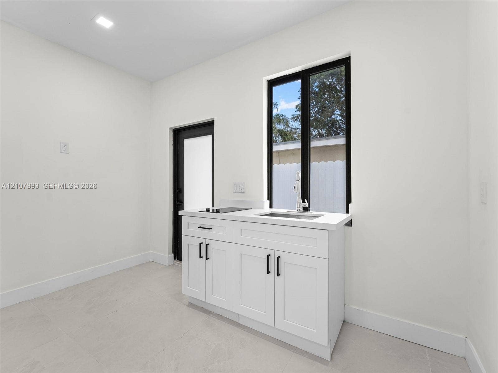 610 NE 164th Terrace, Miami, FL 33162 Shaker-style white cabinetry with matte black hardware, stone-finish countertop, integrated stainless steel sink, and recessed ceiling lighting