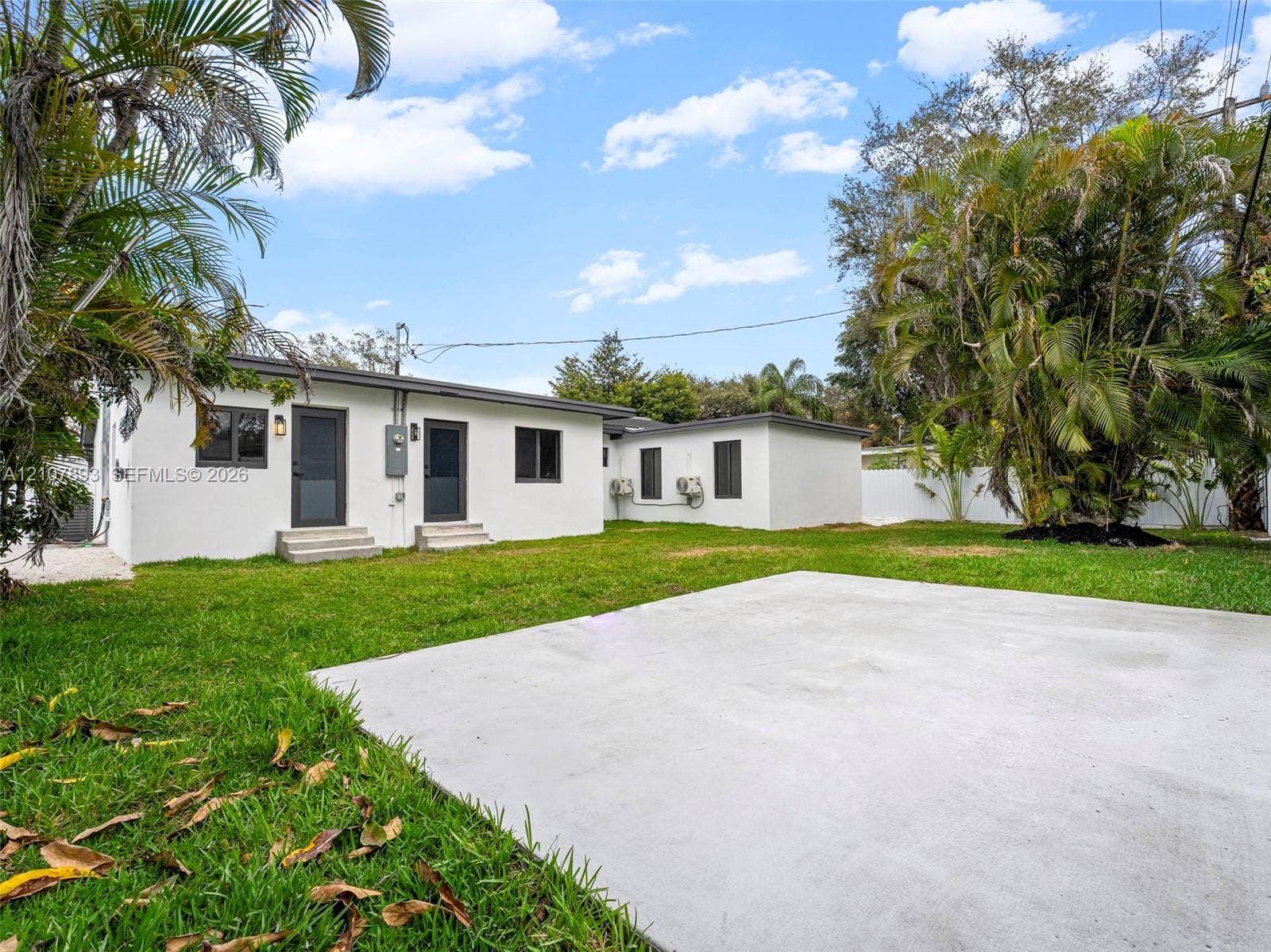 610 NE 164th Terrace, Miami, FL 33162 Expansive backyard featuring a concrete patio, white exterior facade, dark-trimmed windows, and mature palm trees
