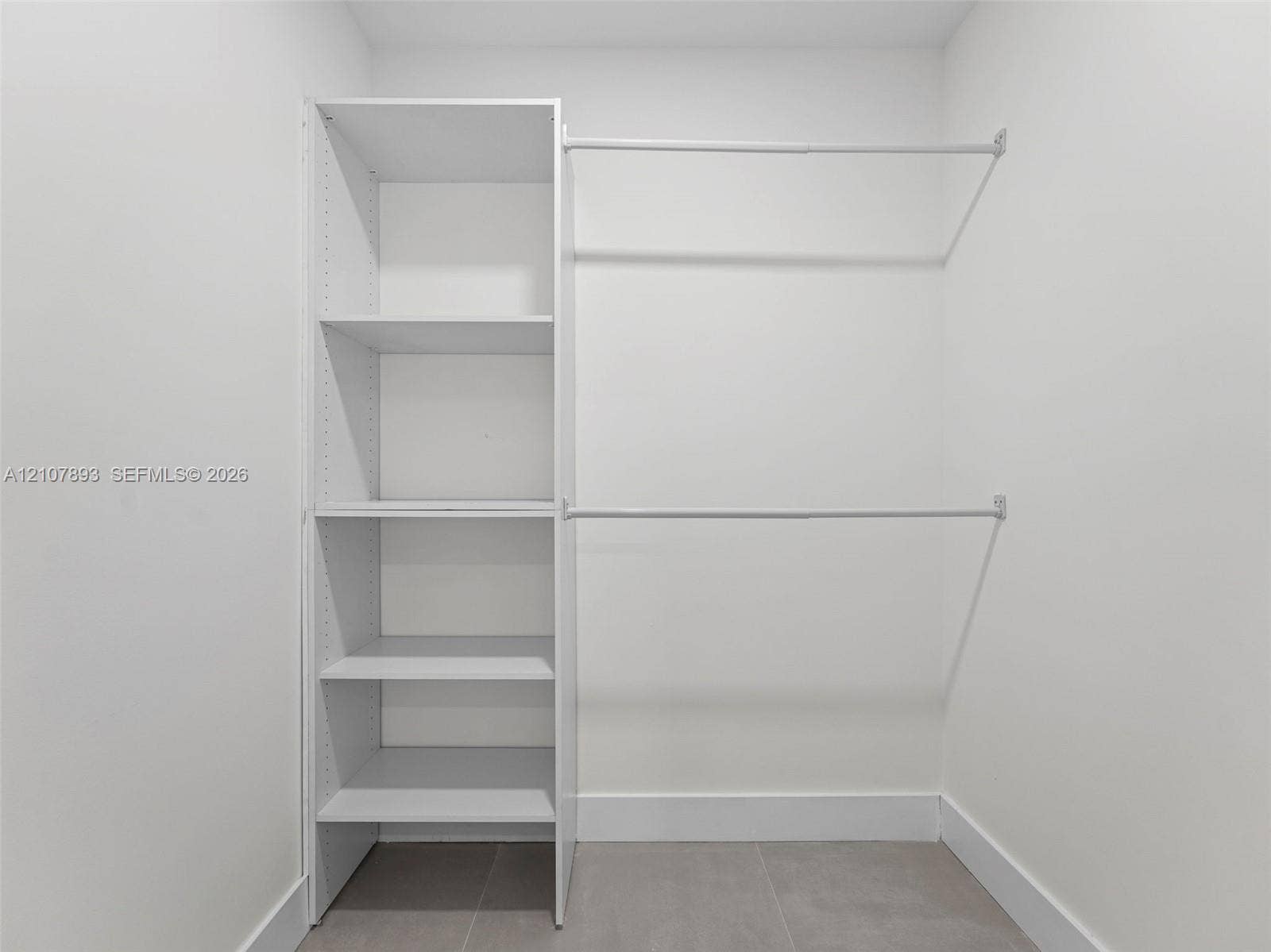 610 NE 164th Terrace, Miami, FL 33162 Walk-in closet featuring white built-in shelving and dual horizontal hanging rods over tile flooring