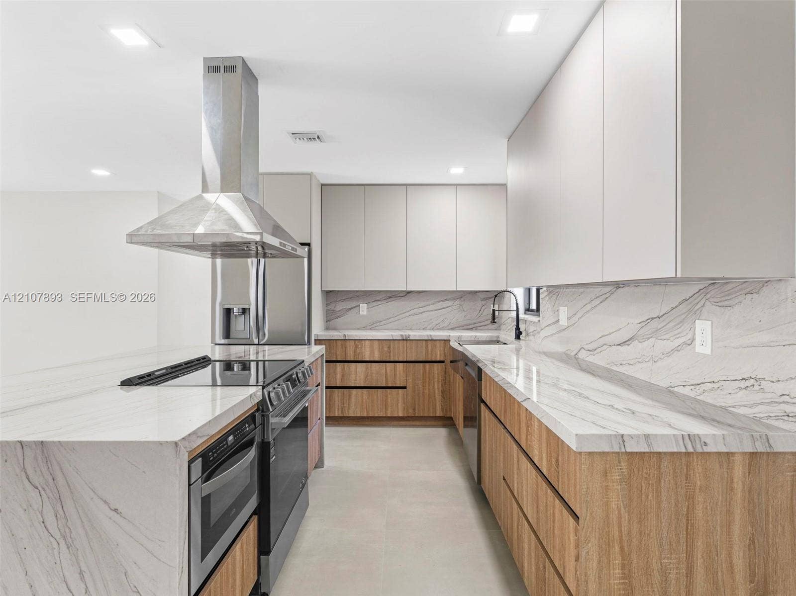 610 NE 164th Terrace, Miami, FL 33162 Modern kitchen featuring flat-panel wood-finish base cabinetry, light-toned upper cabinets, stone-surfaced countertops and backsplash, stainless steel range with integrated hood, and matte black plumbing fixtures