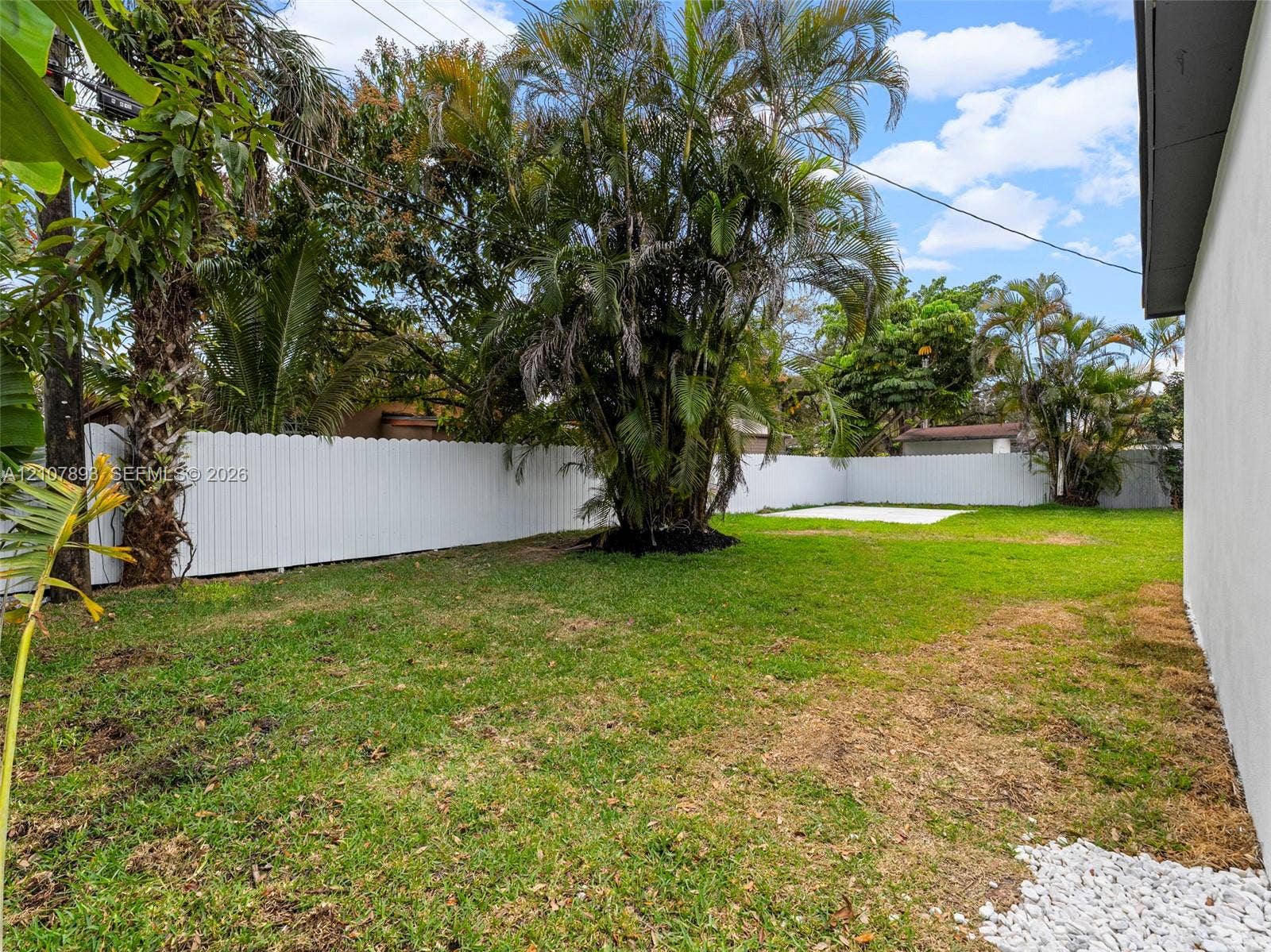610 NE 164th Terrace, Miami, FL 33162 Backyard featuring a grass lawn, white vinyl fencing, mature landscaping, and a concrete patio slab