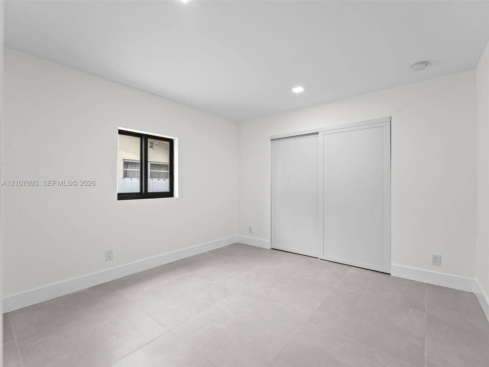 610 NE 164th Terrace, Miami, FL 33162 Neutral-toned large-format tile flooring, recessed ceiling lighting, sliding-panel closet doors, and a window with a black frame