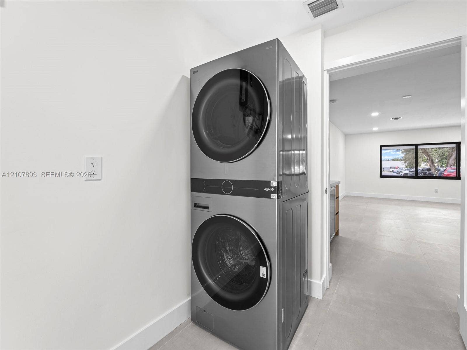 610 NE 164th Terrace, Miami, FL 33162 Stainless steel stacked laundry unit featuring front-loading washer and dryer with integrated digital controls and large-format tile flooring