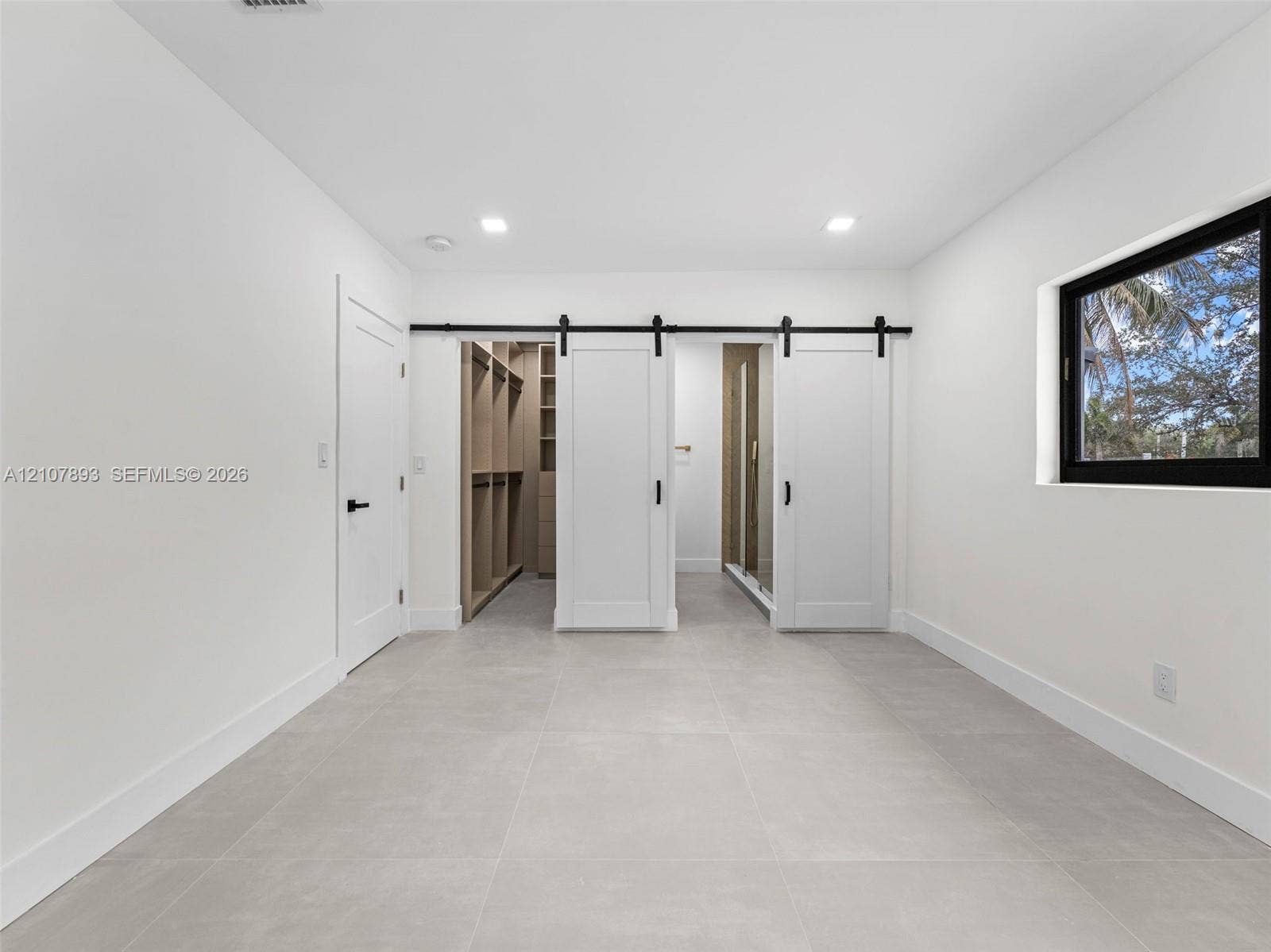 610 NE 164th Terrace, Miami, FL 33162 Large-format tile flooring, dual sliding barn-style doors with matte black hardware, built-in closet storage system, and recessed lighting