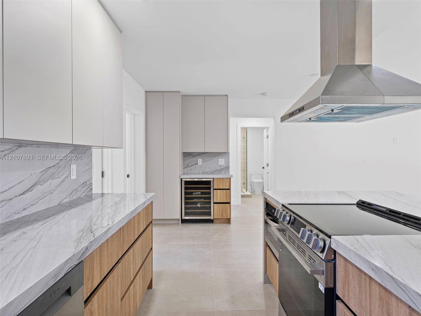 610 NE 164th Terrace, Miami, FL 33162 Kitchen featuring flat-panel wood and matte-finish cabinetry, stone-surface countertops with continuous backsplash, built-in wine refrigeration, stainless steel professional-style range, and wall-mounted stainless steel vent hood