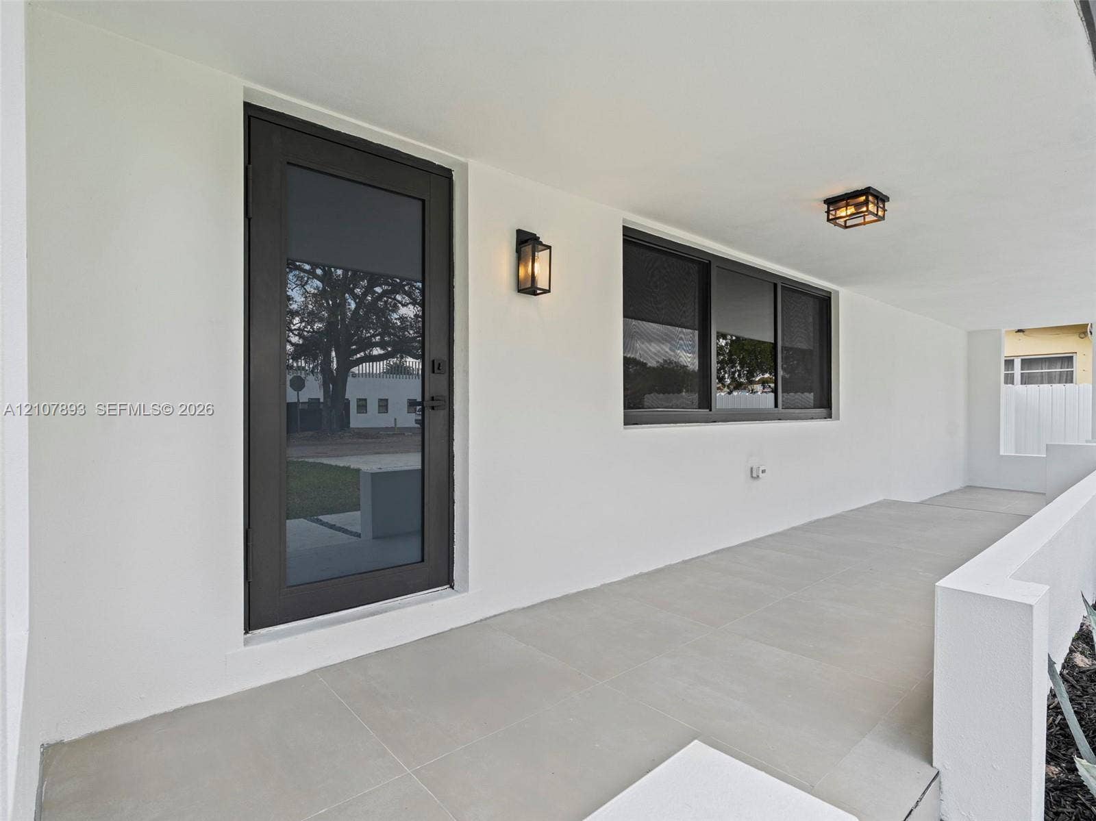 610 NE 164th Terrace, Miami, FL 33162 Covered entryway featuring large-format tile flooring, a full-glass entry door with dark trim, dual wall-mounted lanterns, and a flush-mount ceiling fixture