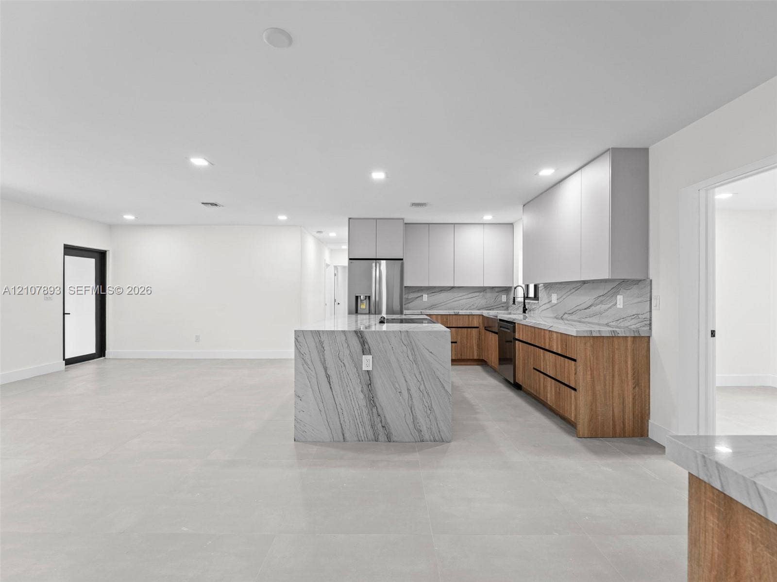 610 NE 164th Terrace, Miami, FL 33162 Modern kitchen featuring a central island with a stone waterfall countertop, wood-finish cabinetry, matte light gray upper cabinets, and a matching stone backsplash