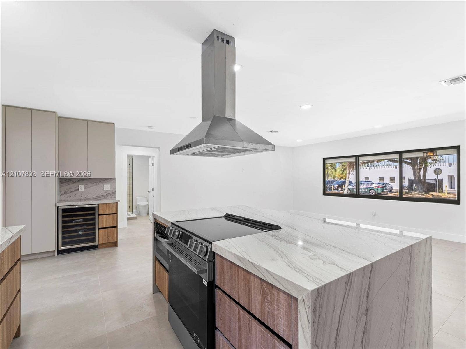 610 NE 164th Terrace, Miami, FL 33162 Kitchen island featuring waterfall-edge stone countertop, stainless steel range, built-in wine refrigerator, custom wood-finish cabinetry, and stainless steel chimney hood